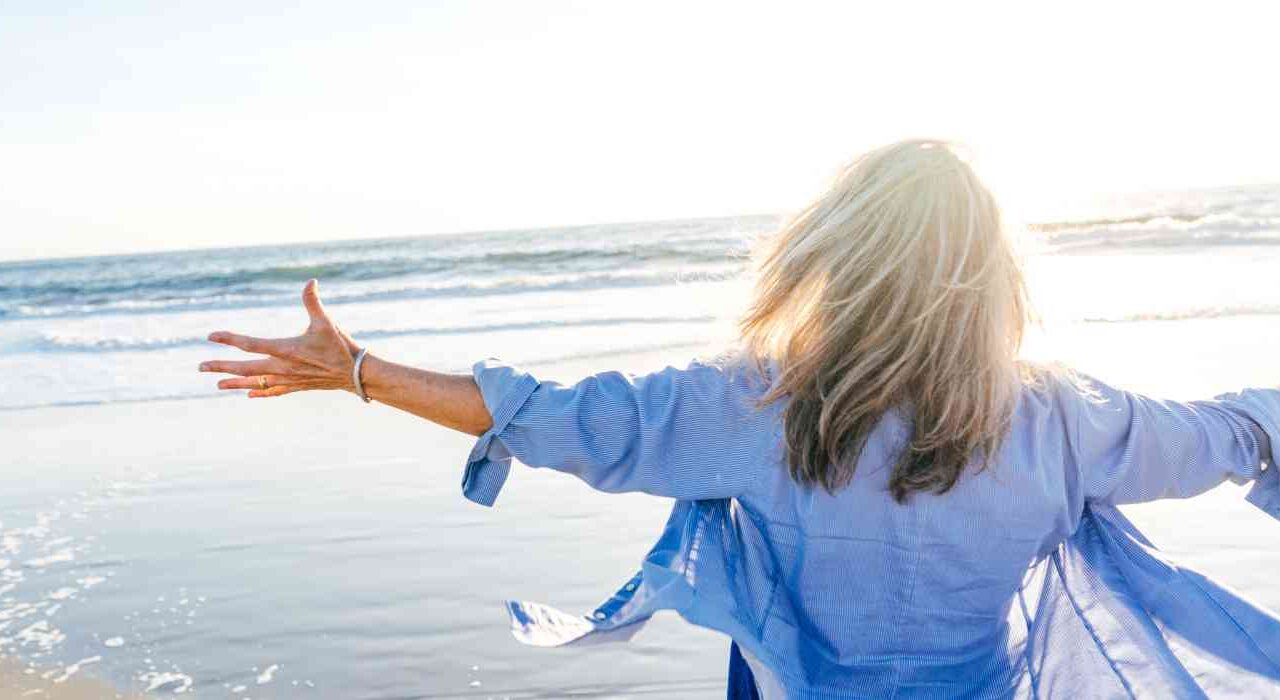 Binge Eating Disorder Banner Image Depicted By Woman Excitedly Gesturing At The Ocean With Wide Open Arms